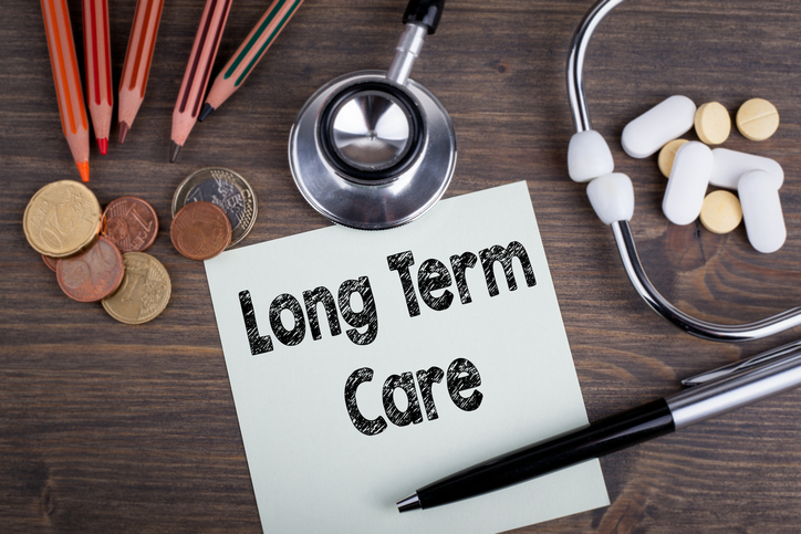 "Long Term Care" written on a sticky note, on a table with a stethoscope and medication.